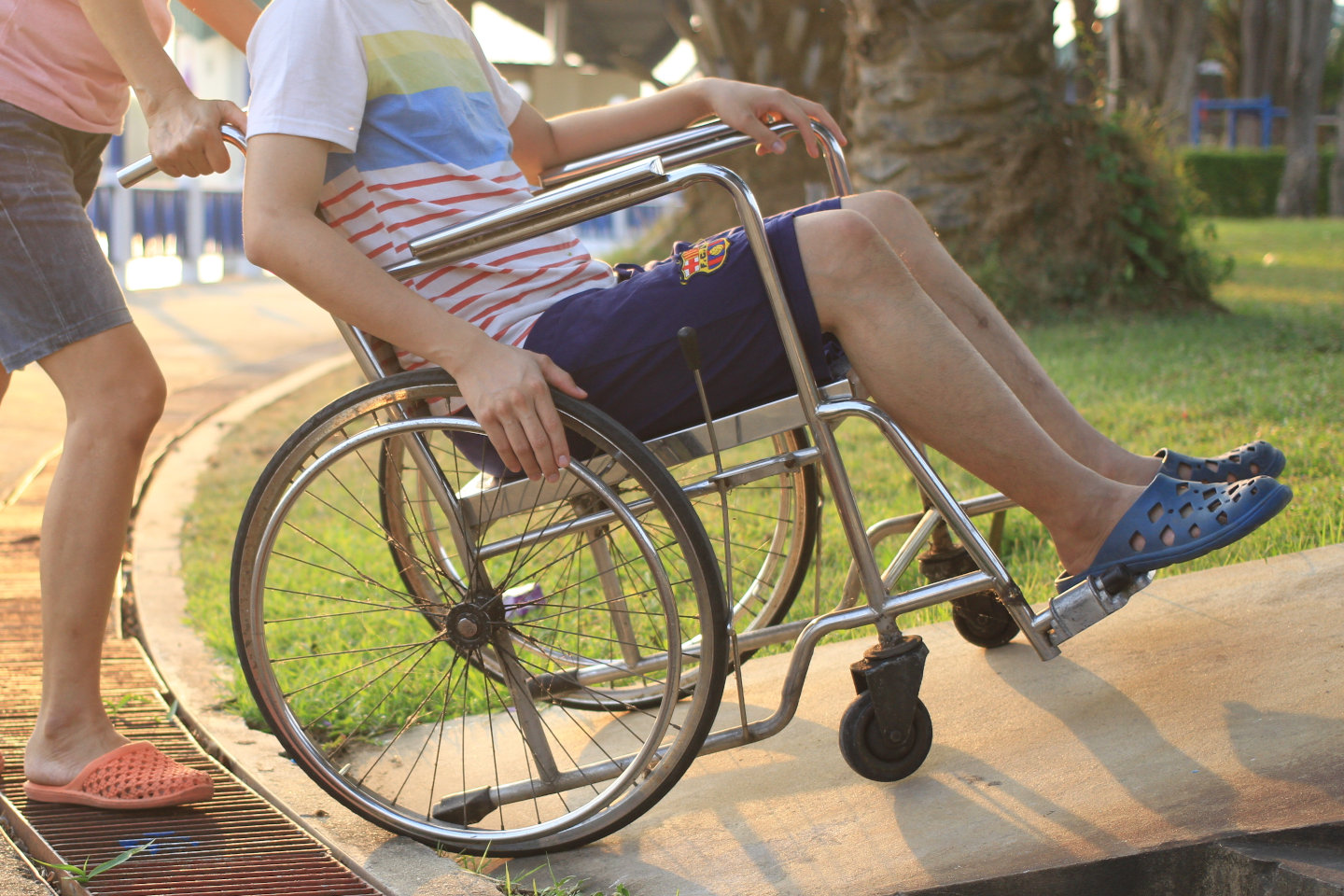 Mother helping her son on wheelchair up the ramp in the park with sunset in background, warm filter