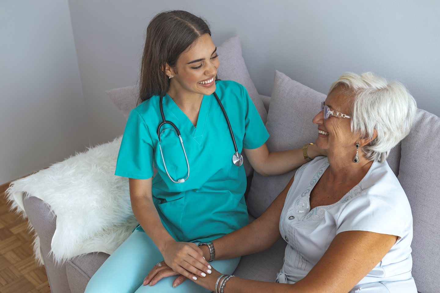 Young caring lovely caregiver and happy ward. Image of caregiver and senior resting in the living room. Smiling caregiver taking care of a happy elderly woman